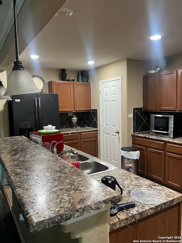 kitchen featuring decorative backsplash, black fridge with ice dispenser, and an island with sink