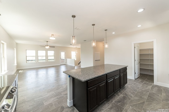 kitchen with pendant lighting, light stone counters, ceiling fan, and a kitchen island