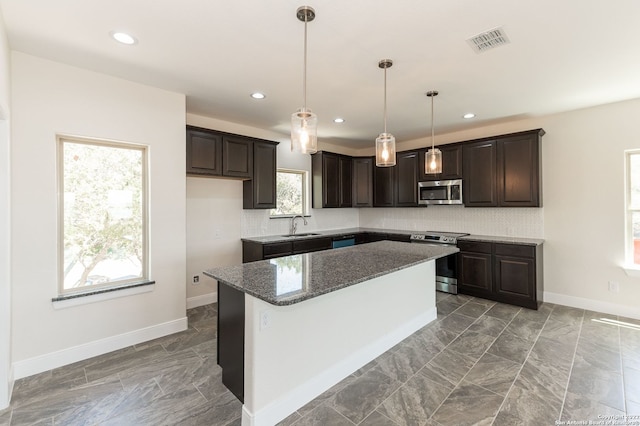 kitchen with sink, hanging light fixtures, dark stone countertops, a kitchen island, and appliances with stainless steel finishes