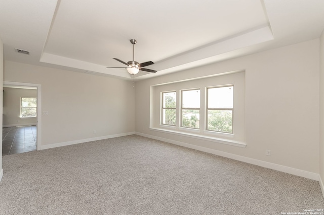 carpeted spare room with a tray ceiling and ceiling fan