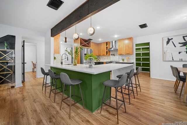 kitchen featuring a breakfast bar, light hardwood / wood-style flooring, hanging light fixtures, and wall chimney exhaust hood