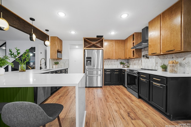 kitchen with stainless steel appliances, wall chimney range hood, kitchen peninsula, pendant lighting, and light wood-type flooring