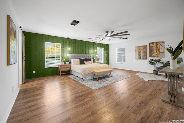 bedroom with wood-type flooring, a barn door, and ceiling fan