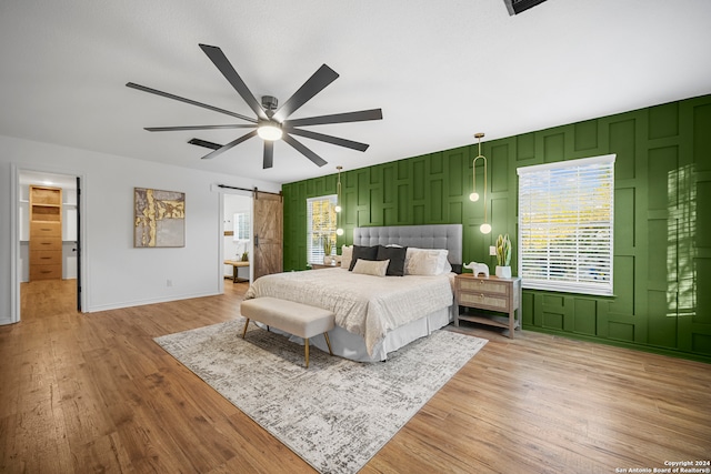 bedroom featuring connected bathroom, a barn door, ceiling fan, and light hardwood / wood-style floors