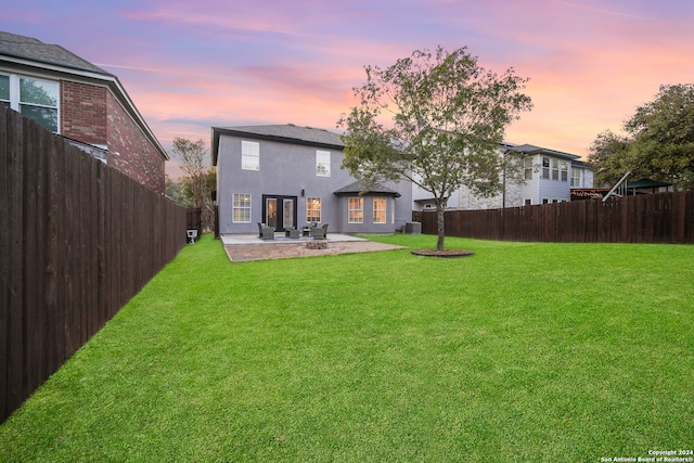 back house at dusk with central AC unit, a yard, and a patio