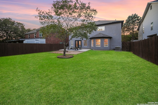 back house at dusk with a lawn, central AC, and a patio area