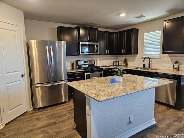 kitchen featuring light stone counters, stainless steel appliances, sink, hardwood / wood-style floors, and a kitchen island