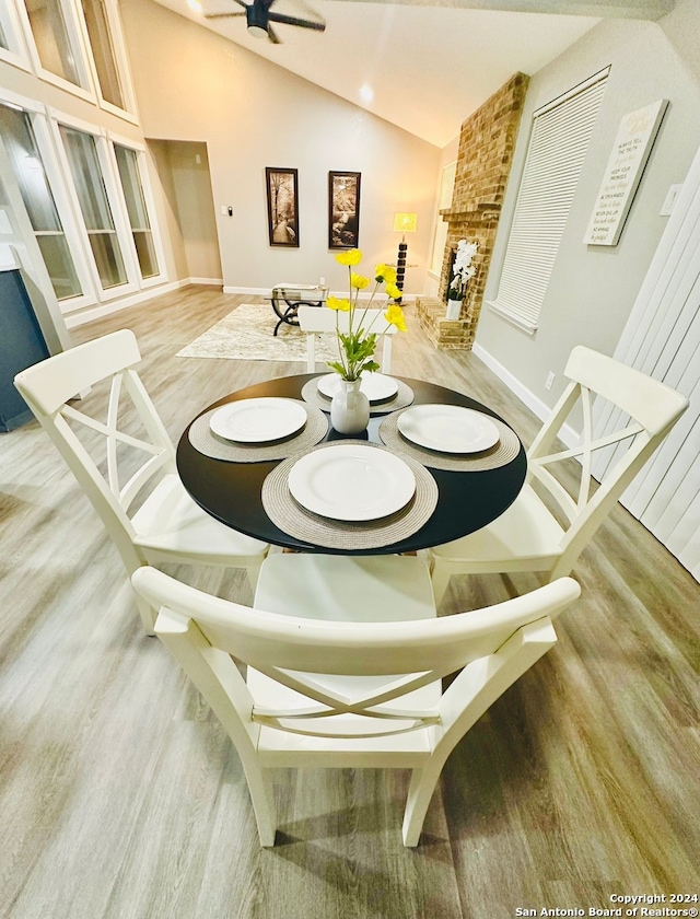 dining space with a stone fireplace, ceiling fan, light hardwood / wood-style floors, and vaulted ceiling