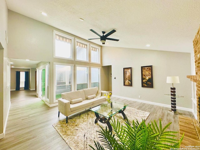 living room with ceiling fan, high vaulted ceiling, a textured ceiling, and light wood-type flooring