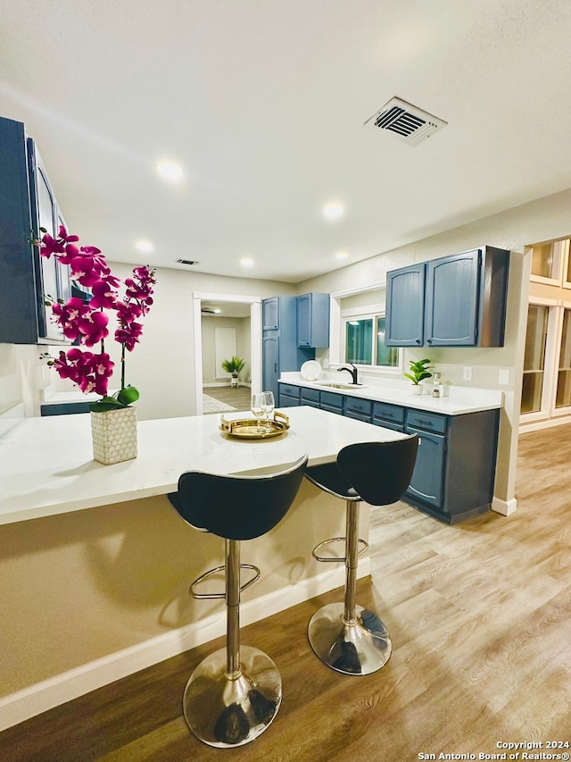 kitchen featuring a breakfast bar, sink, light wood-type flooring, and blue cabinetry