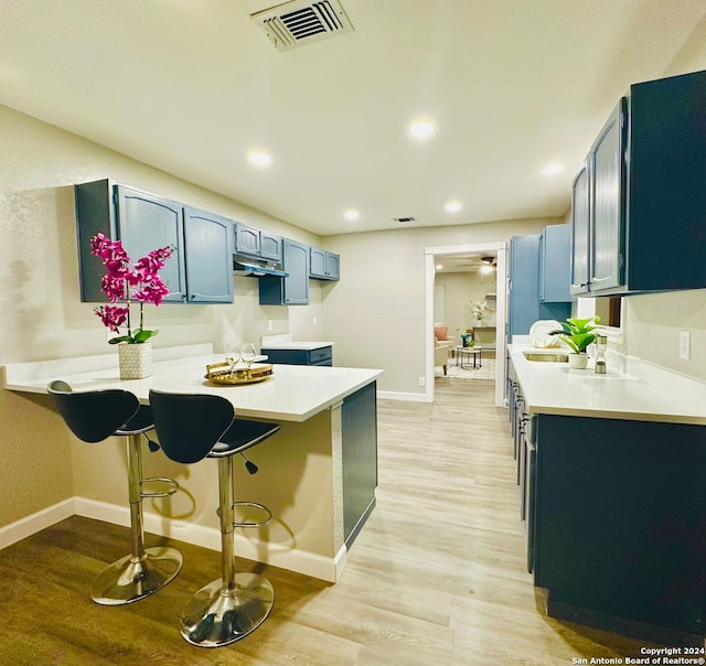 kitchen featuring a kitchen bar, light hardwood / wood-style flooring, blue cabinets, and sink