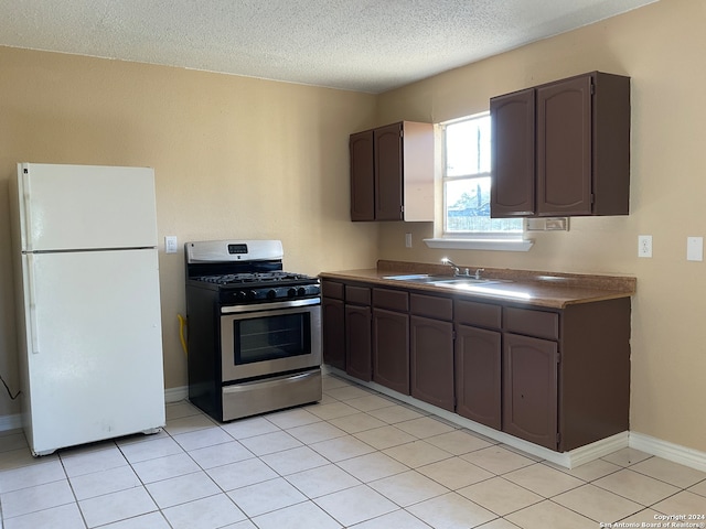 kitchen with sink, stainless steel gas stove, a textured ceiling, white fridge, and dark brown cabinetry