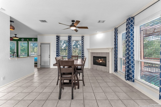 tiled dining room with plenty of natural light, ceiling fan, ornamental molding, and a tiled fireplace