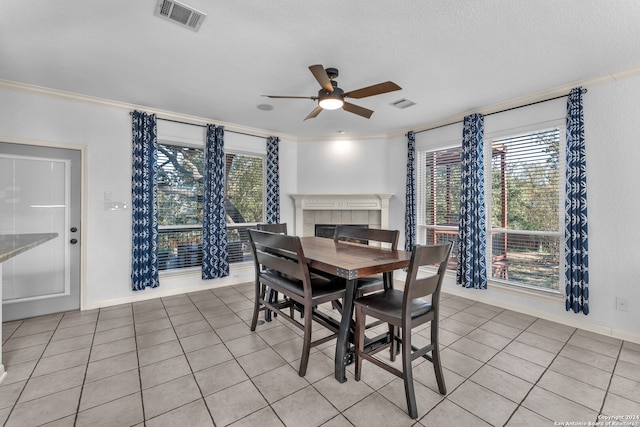 dining area with a textured ceiling, ceiling fan, crown molding, a fireplace, and light tile patterned flooring