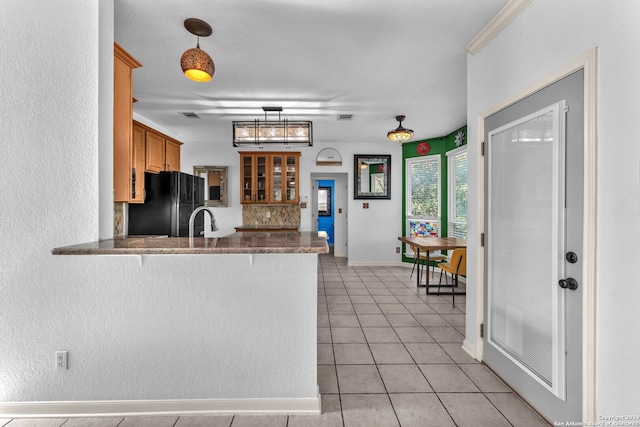 kitchen with kitchen peninsula, black fridge, sink, light tile patterned floors, and decorative light fixtures