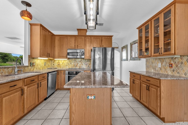 kitchen featuring light stone countertops, sink, pendant lighting, a kitchen island, and appliances with stainless steel finishes