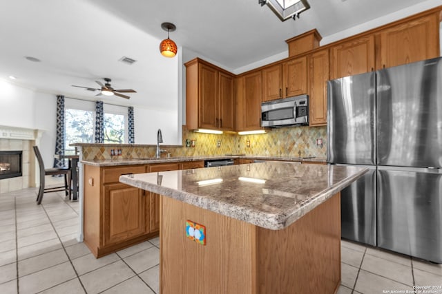 kitchen featuring light tile patterned flooring, a tile fireplace, ceiling fan, a kitchen island, and stainless steel appliances