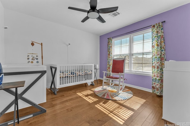 bedroom featuring hardwood / wood-style floors, ceiling fan, and a crib