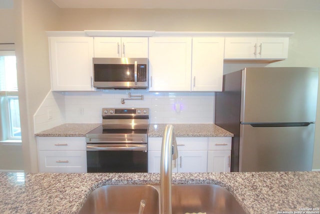 kitchen featuring white cabinetry, sink, light stone counters, backsplash, and appliances with stainless steel finishes