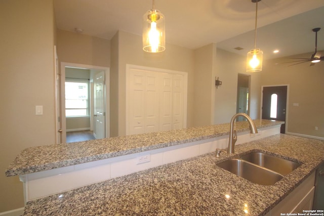 kitchen with decorative light fixtures, ceiling fan, light stone countertops, and sink