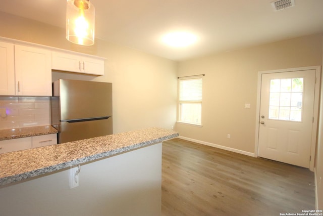 kitchen featuring white cabinets, decorative backsplash, light stone countertops, wood-type flooring, and stainless steel refrigerator