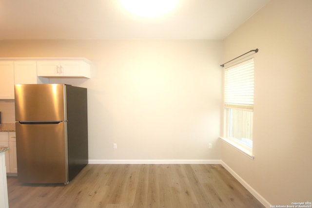 kitchen with white cabinets, light hardwood / wood-style flooring, and stainless steel refrigerator