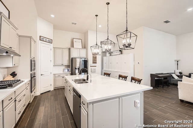 kitchen with stainless steel appliances, dark wood-type flooring, sink, decorative light fixtures, and an island with sink