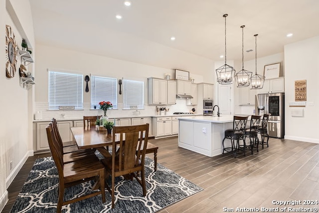 kitchen featuring a center island with sink, sink, hardwood / wood-style flooring, a kitchen bar, and stainless steel appliances