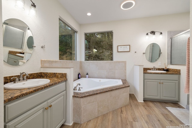 bathroom with wood-type flooring, vanity, and tiled tub