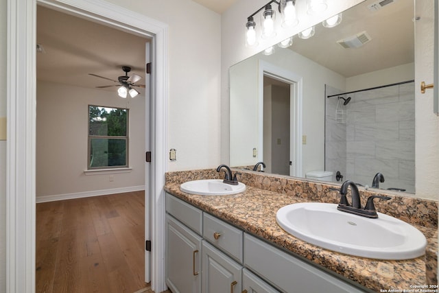 bathroom with a tile shower, vanity, ceiling fan, hardwood / wood-style flooring, and toilet