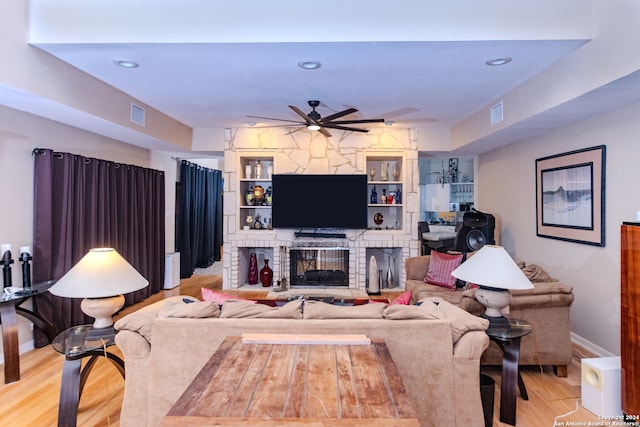 living room featuring ceiling fan, a large fireplace, and light wood-type flooring