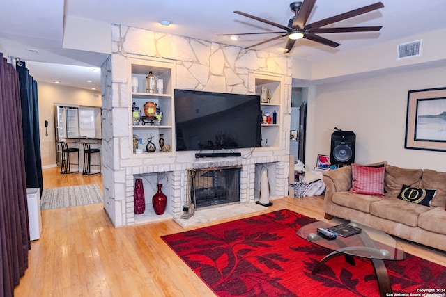 living room featuring hardwood / wood-style flooring, ceiling fan, a fireplace, and built in shelves