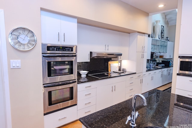 kitchen with double oven, electric stovetop, sink, dark stone countertops, and white cabinets