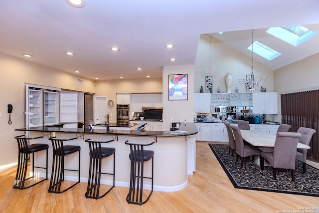 kitchen featuring a skylight, a breakfast bar, stainless steel double oven, light hardwood / wood-style floors, and white cabinetry