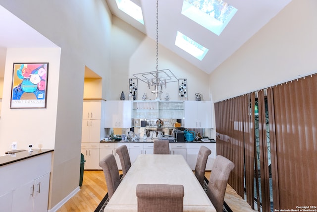 dining room featuring a skylight, an inviting chandelier, high vaulted ceiling, and light wood-type flooring