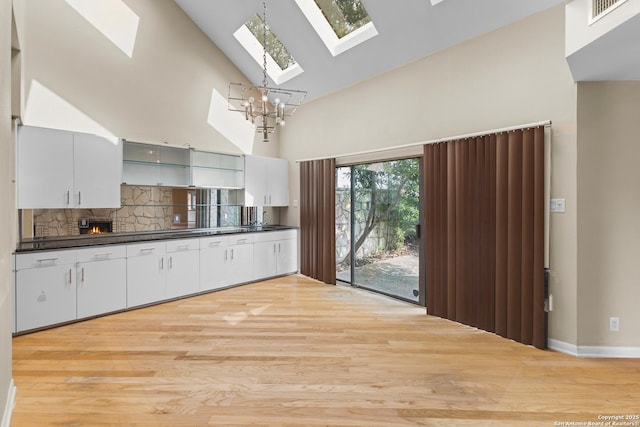 206 Bluff Holw, San Antonio, TX 78216 - kitchen featuring a skylight, high vaulted ceiling, dark countertops, light wood-style flooring, and decorative backsplash