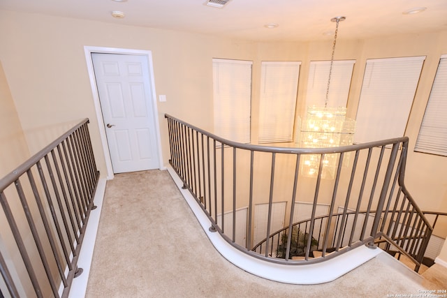 hallway featuring light colored carpet and a notable chandelier