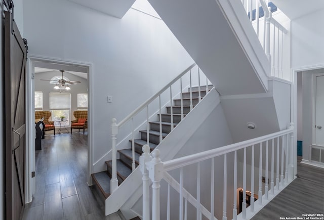 stairs with ceiling fan, a barn door, wood-type flooring, and a towering ceiling