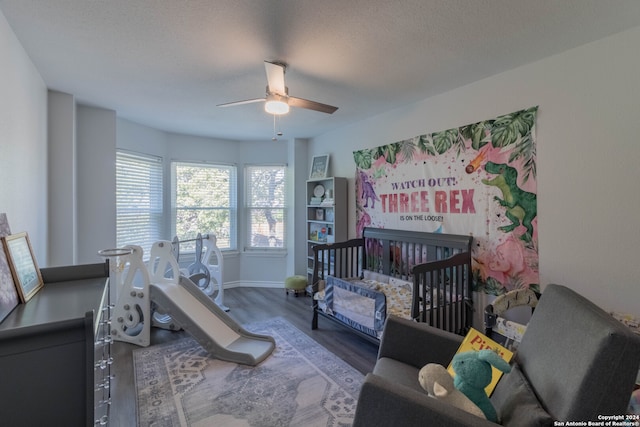 bedroom with a crib, a textured ceiling, ceiling fan, and dark wood-type flooring