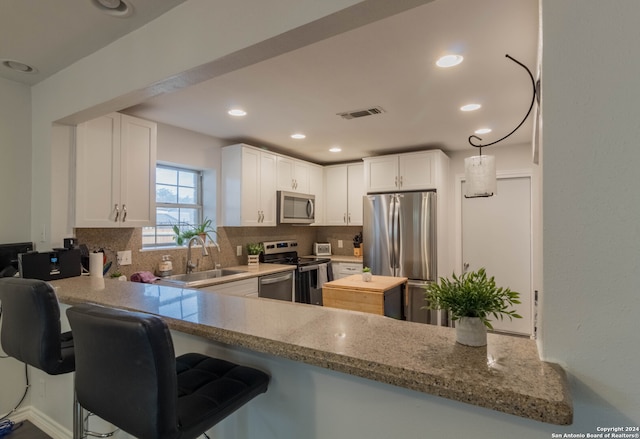 kitchen featuring kitchen peninsula, appliances with stainless steel finishes, decorative backsplash, and white cabinetry