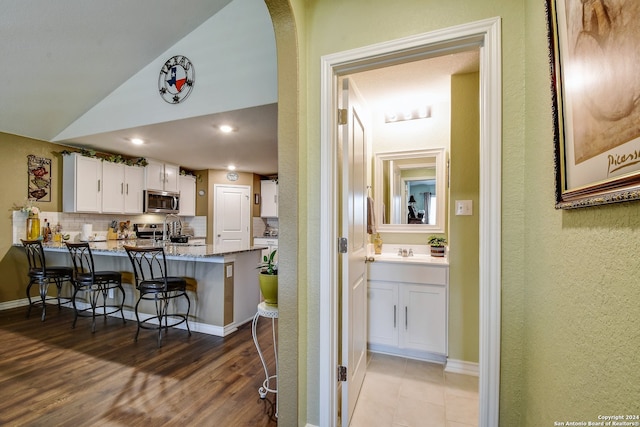 kitchen featuring kitchen peninsula, light stone counters, a breakfast bar, stainless steel appliances, and white cabinetry