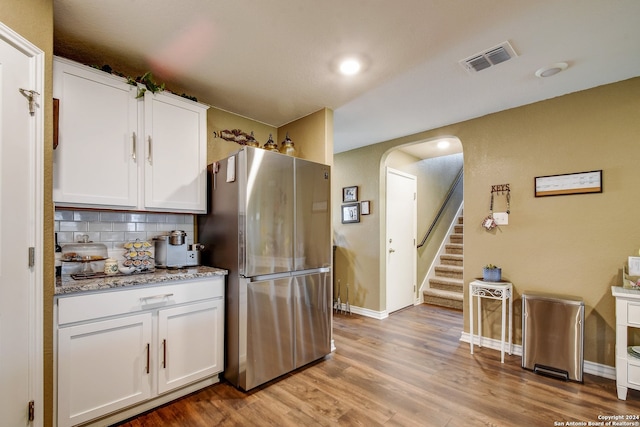 kitchen with stainless steel fridge, tasteful backsplash, light stone counters, light hardwood / wood-style flooring, and white cabinets