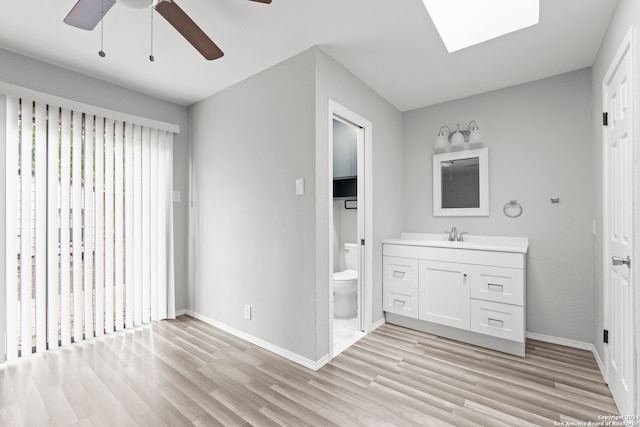 bathroom featuring a skylight, vanity, ceiling fan, wood-type flooring, and toilet