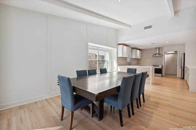 dining area featuring beamed ceiling, light wood-type flooring, and sink