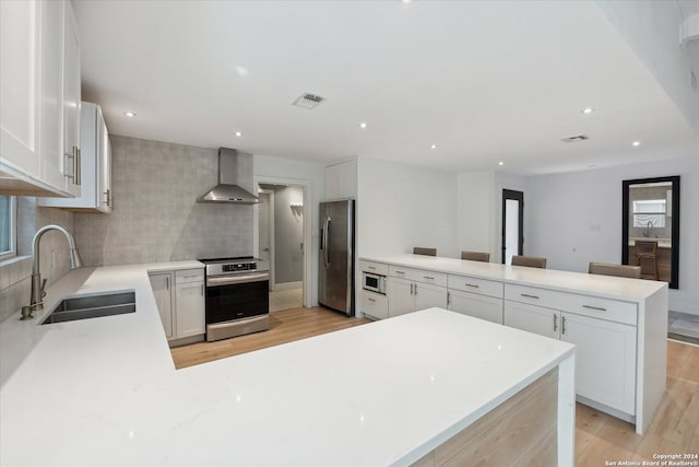 kitchen with wall chimney range hood, sink, light wood-type flooring, appliances with stainless steel finishes, and white cabinetry