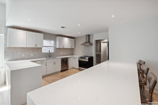 kitchen with wall chimney exhaust hood, white cabinetry, sink, and appliances with stainless steel finishes