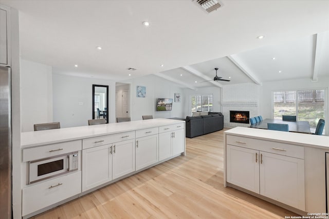 kitchen with lofted ceiling with beams, light hardwood / wood-style flooring, a wealth of natural light, and a brick fireplace