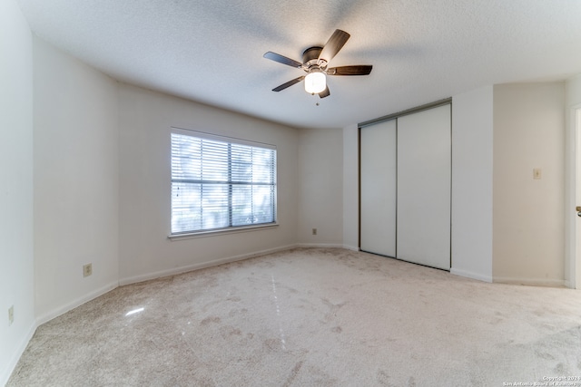 unfurnished bedroom with ceiling fan, a closet, light carpet, and a textured ceiling