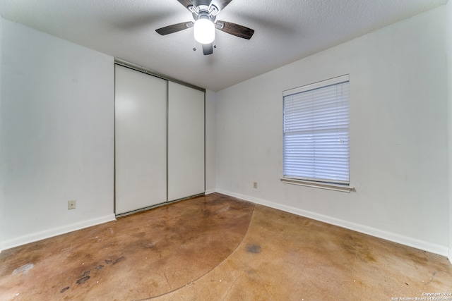 unfurnished bedroom with ceiling fan, concrete flooring, a textured ceiling, and a closet