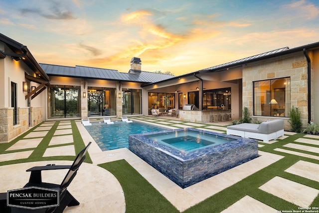 pool at dusk featuring a patio area and an in ground hot tub